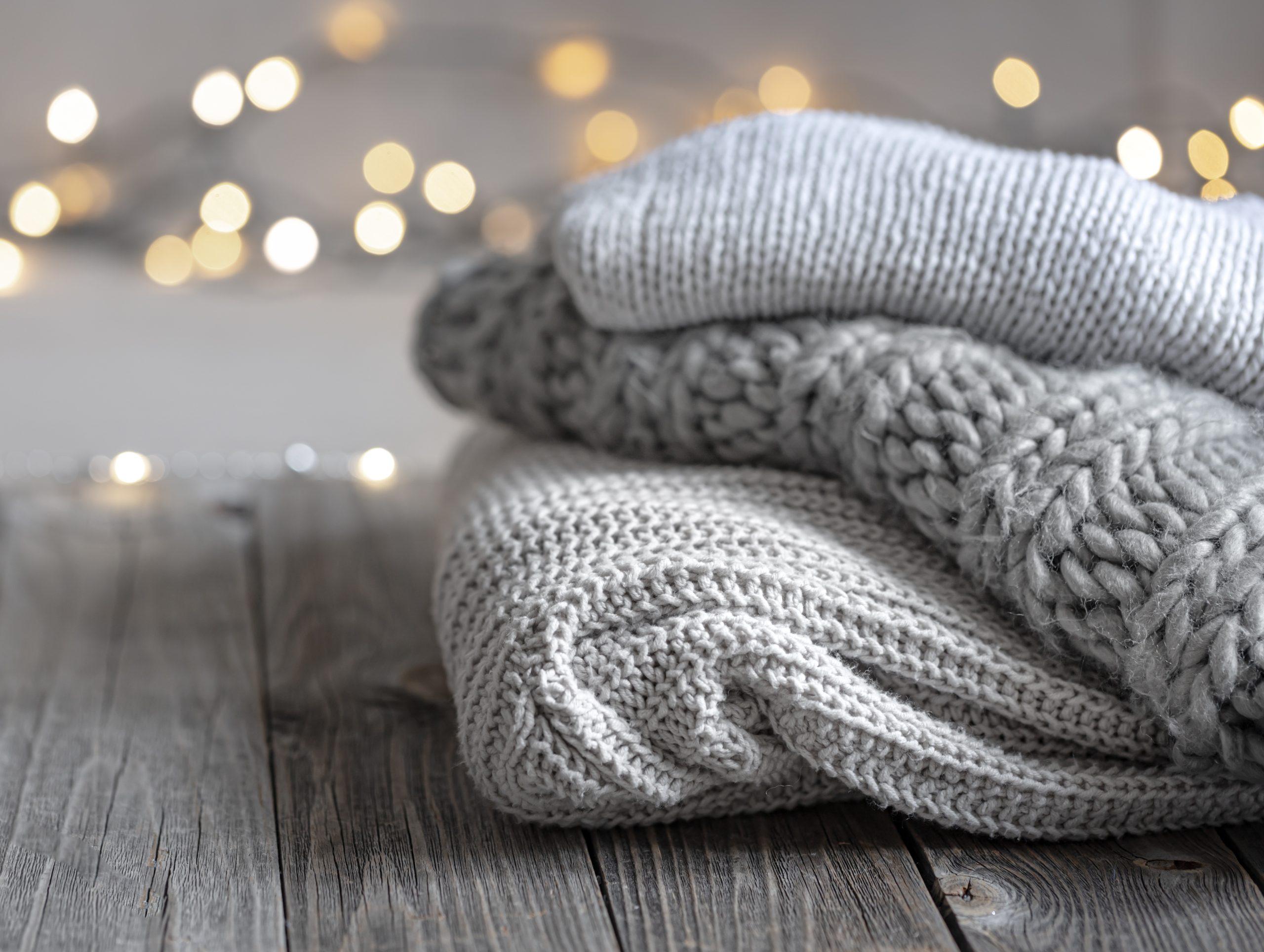 Cozy winter background with a stack of knitted sweaters and lights,